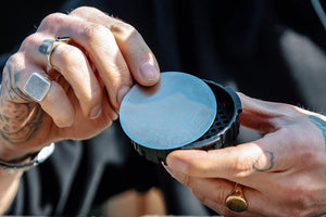 The image shows someone holding a metal filter for an AeroPress coffee maker. The AeroPress is a popular device for brewing coffee, and metal filters like the one in the picture can be used as an alternative to the standard paper filters. They are reusable and often favoured by those looking for a more environmentally friendly option or a slightly different flavour profile in their coffee. The metal filter allows more oils and fine particles to pass through, resulting in a fuller-bodied cup of coffee.