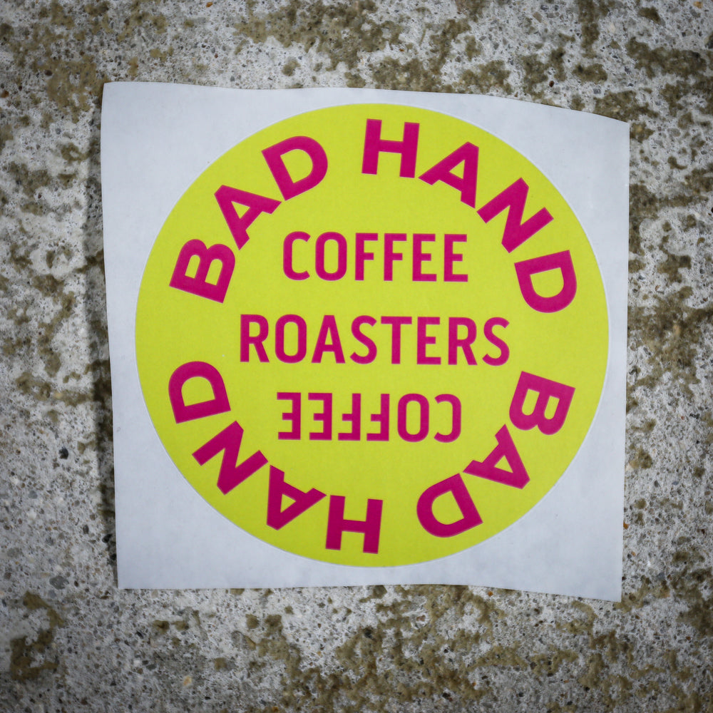 Bad Hand Coffee sticker pack, contains five waterproof stickers of various styles. Sticker four, round, with pink text on a yellow background.